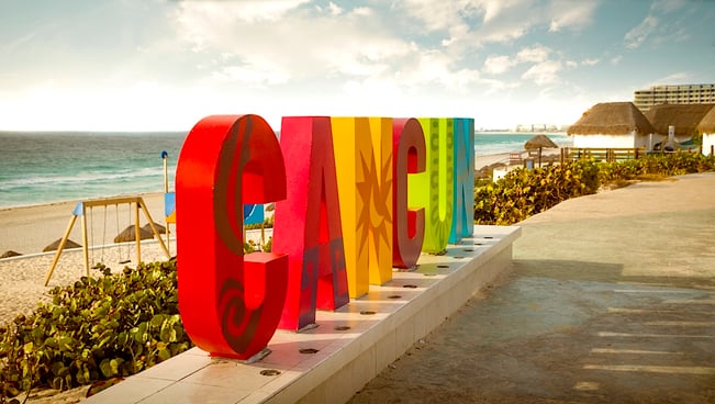 Cancún sign with a sandy beach and turquoise Caribbean water in the background