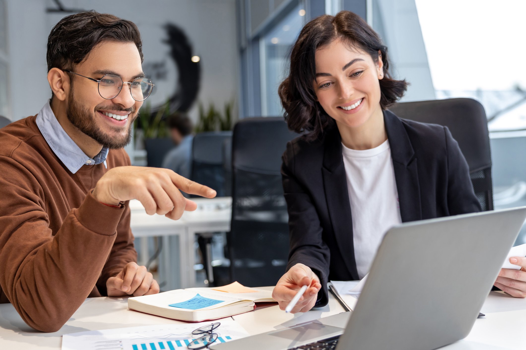 Young man showing female co-worker how to use laptop in office.
