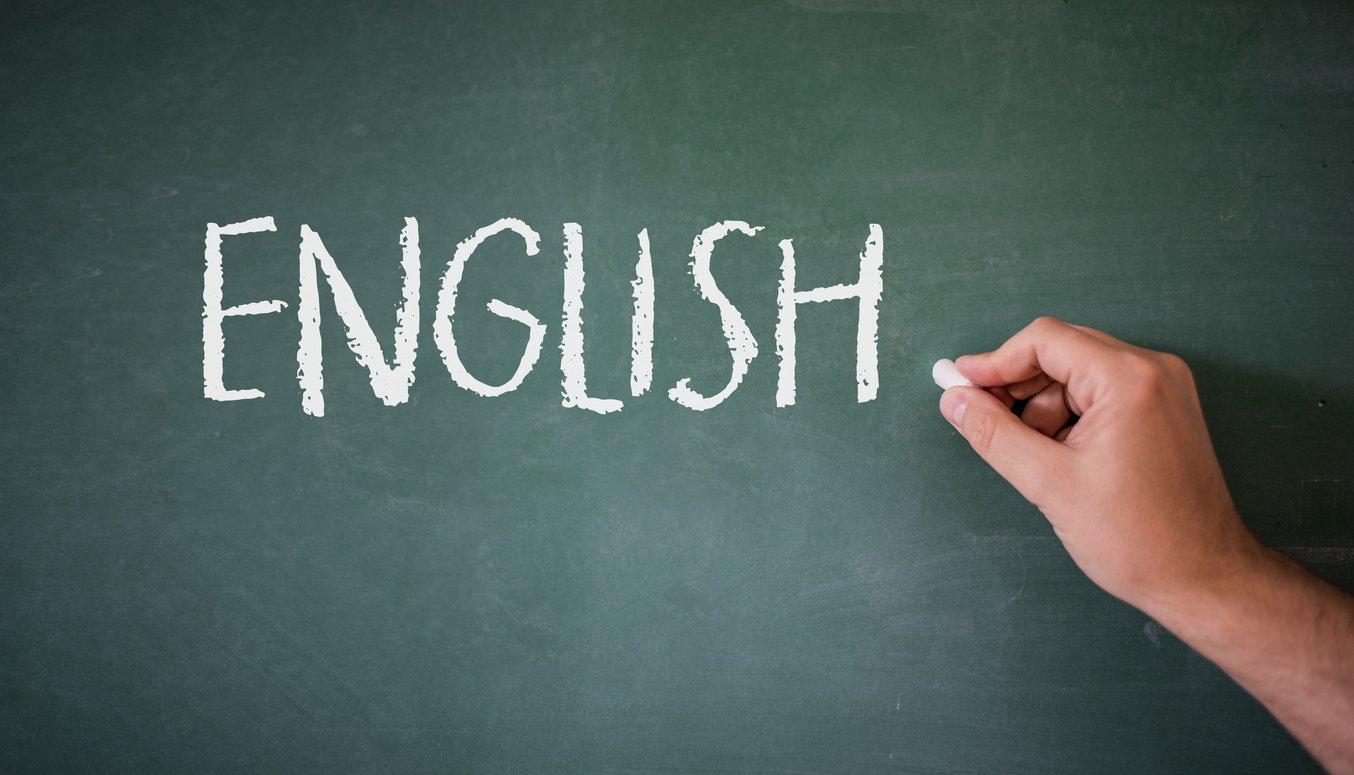 Teacher writing English idioms on a green chalkboard with white chalk during an ESL class.